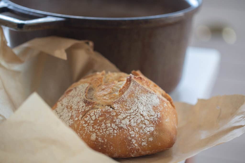 A small batch sourdough loaf on parchment paper with a dutch oven in the background