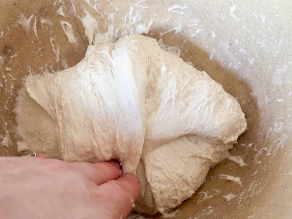 Woman folding bread dough back in after a stretch and fold for small batch sourdough bread