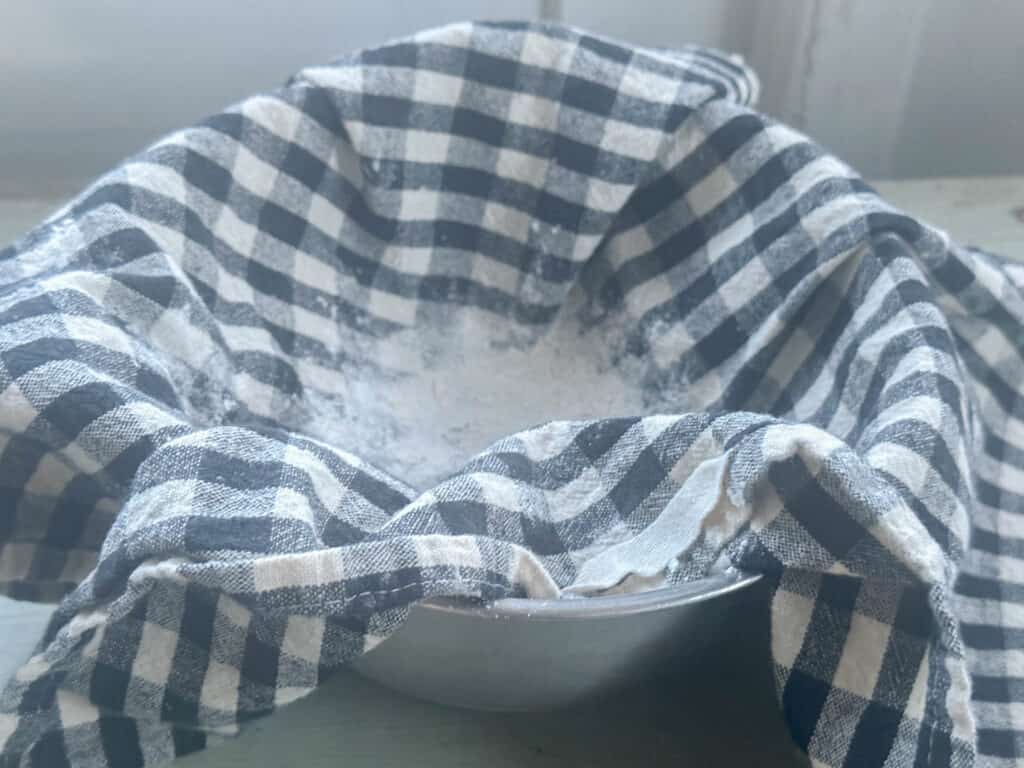 A small bowl lined with a blue and white checkered tea towel dusted with flour