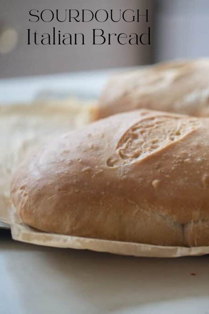 two loaves of fresh baked sourdough Italian bread on parchment paper on white countertop 