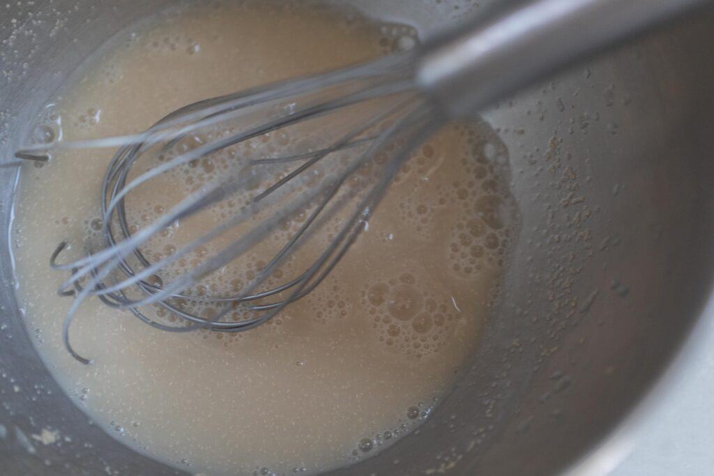 water and commercial yeast in a metal bowl with a whisk in the bowl