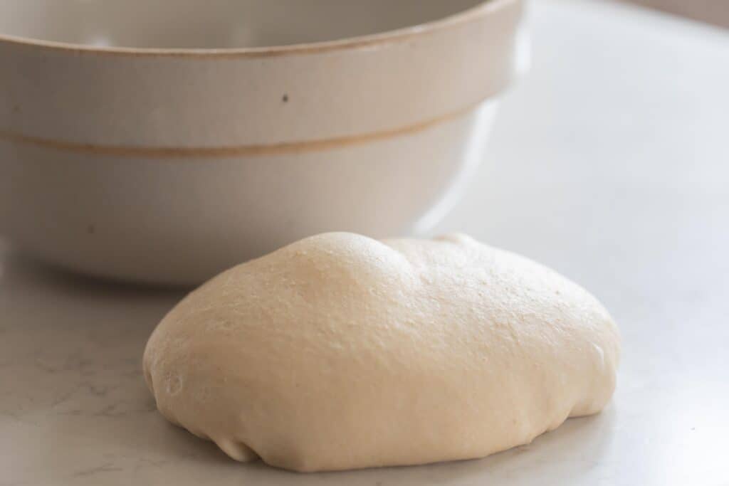 risen roll dough on a white counter with a ironstone bowl