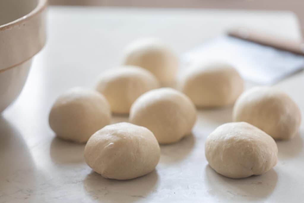 rolls shaped on a white countertop with a bench scraper in the background