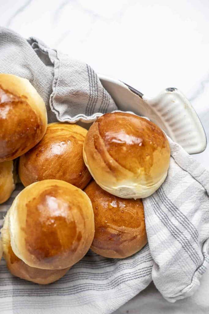 six sourdough discard dinner rolls in a dish lined with a cream and blue plaid towel