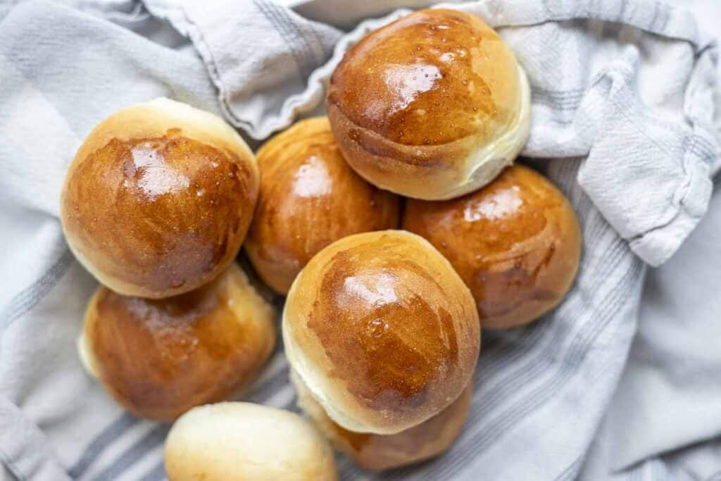 overhead photo sourdough discard rolls in a dish lined with a blue and white plaid towel