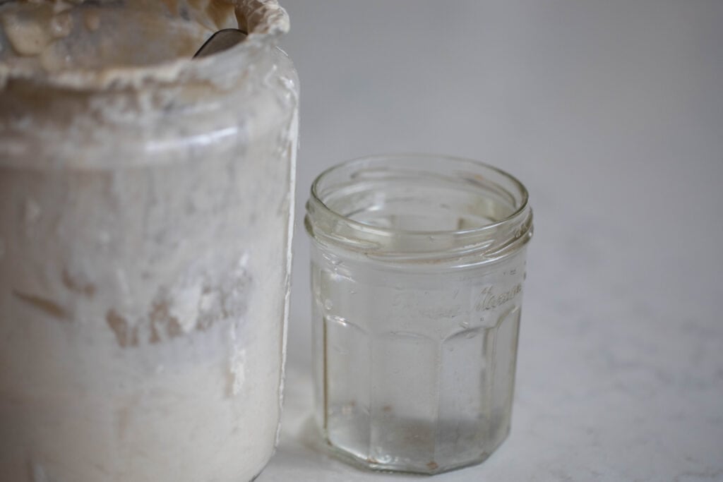 jar of water and a large jar of sourdough starter on a white countertop 