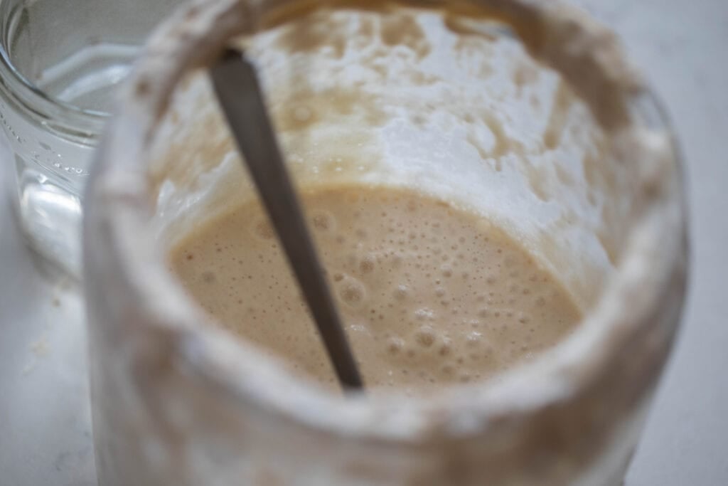 A jar of sourdough starter with a spoon on a white countertop 