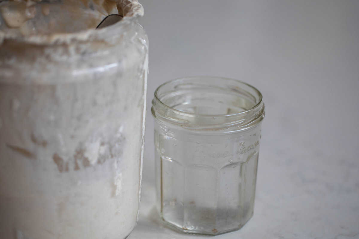 jar of water and a large jar of sourdough starter on a white countertop