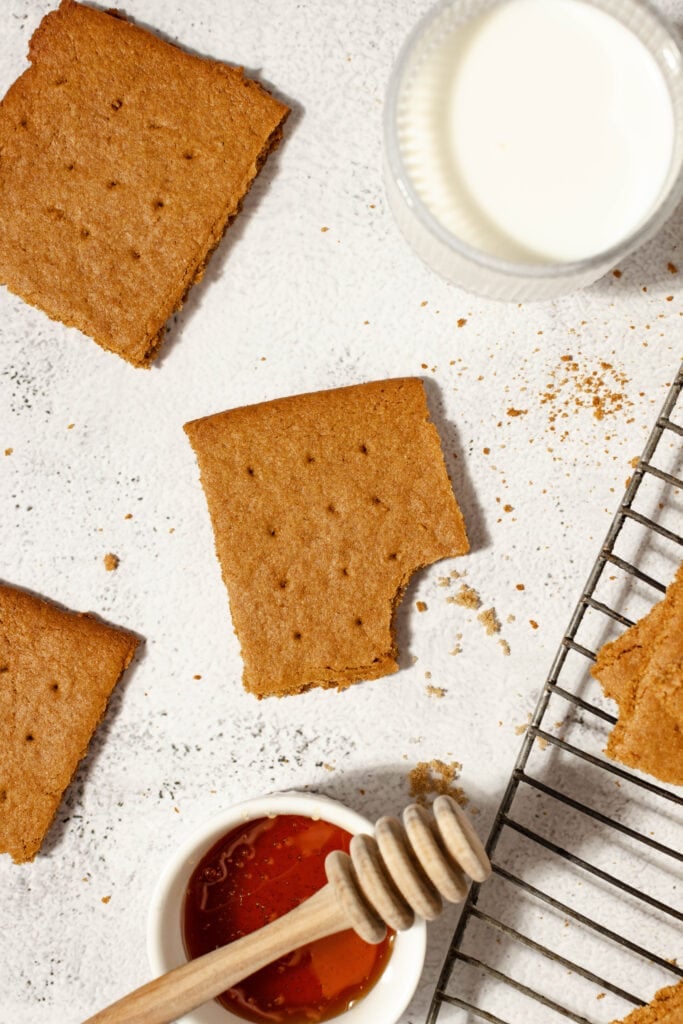 graham cracker with a bite taken out surrounded by honey, milk, more graham crackers, and a wire cooking rack