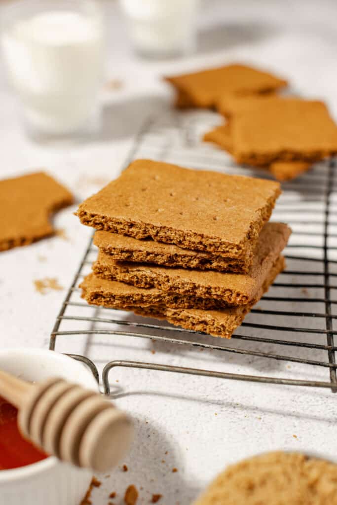 stack of homemade sourdough graham crackers on a wire rack surrounded by honey, milk, and more crackers