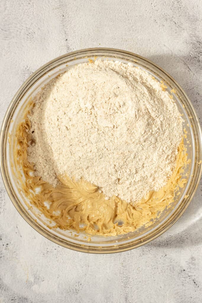 adding flour to a butter sugar mixer in a glass bowl