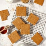 overhead photo of graham crackers spread allover a countertop and wire cooling rack with glasses of milk and honey surrounding the crackers