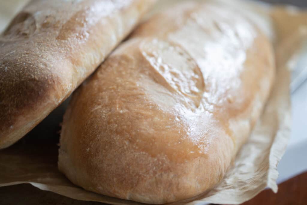 two loaves of sourdough Italian bread stacked on each other on parchment paper