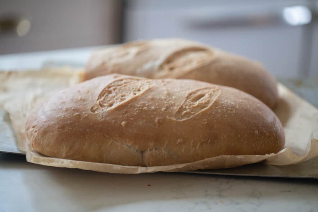 two loaves of sourdough Italian Bread on parchment paper on a white countertop