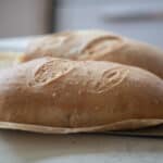 two loaves of sourdough Italian Bread on parchment paper on a white countertop