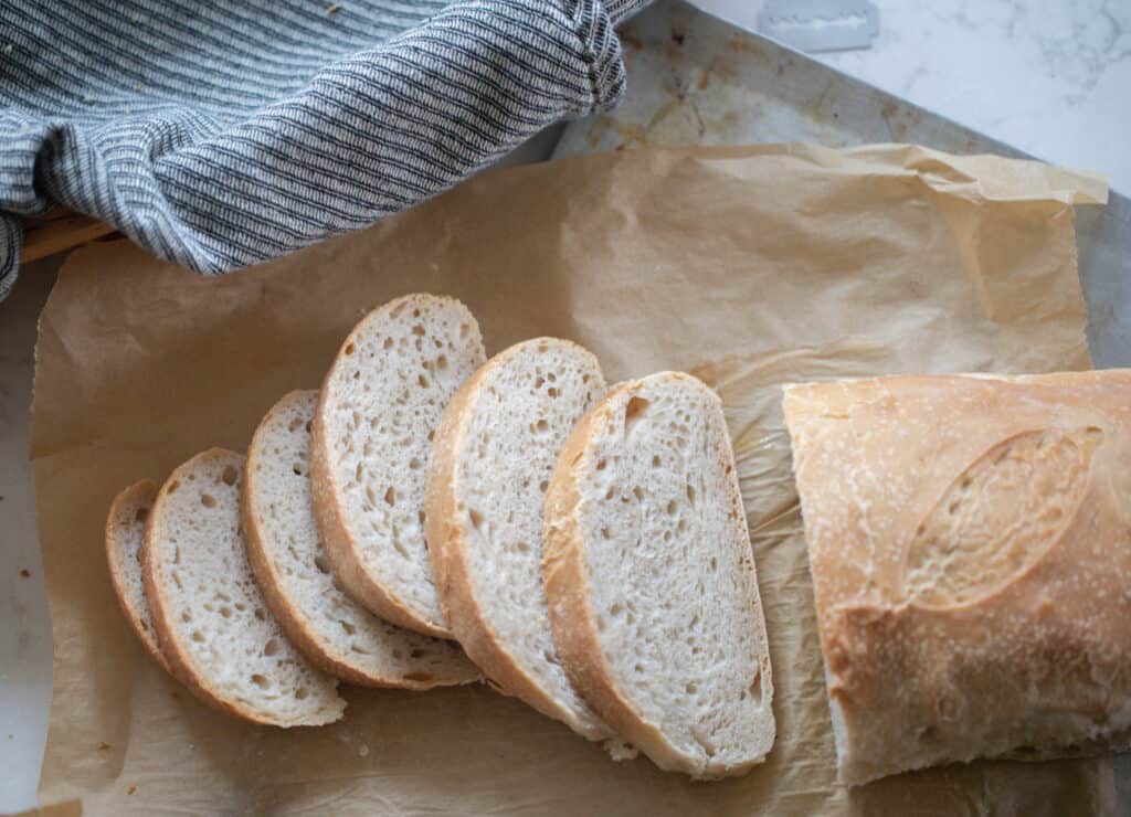 a loaf of sourdough Italian bread with 5 slices off the loaf laying next to the loaf on parchment paper