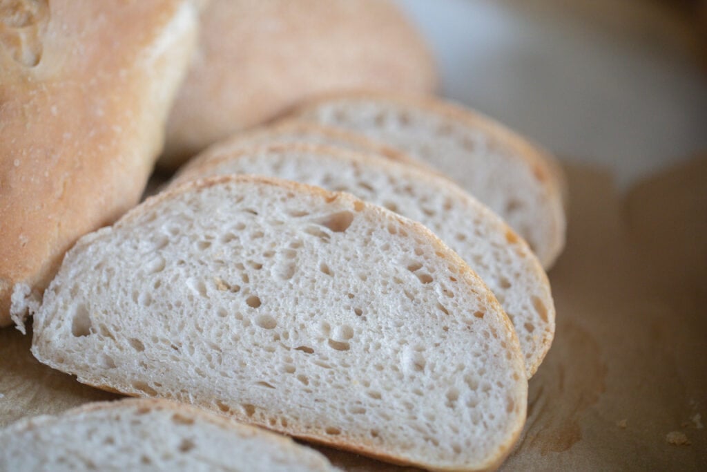 slices of sourdough Italian bread next to a loaf of bread on parchment paper