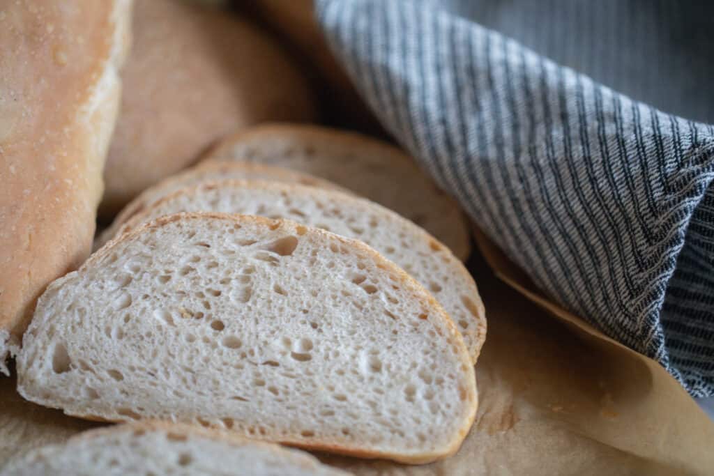 three slices of sourdough Italian bread on parchment paper with a blue and white stripped towel in the back right corner