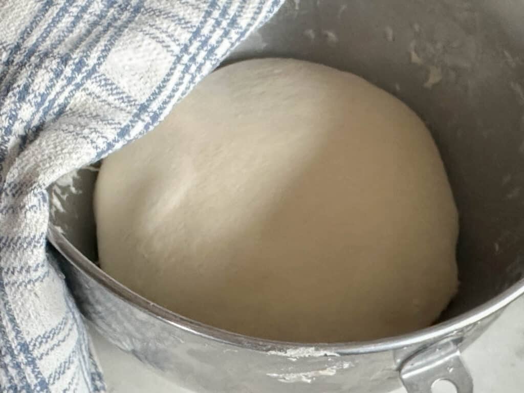 smooth bread dough in a stand mixer bowl. A blue and white plaid towel is on the right