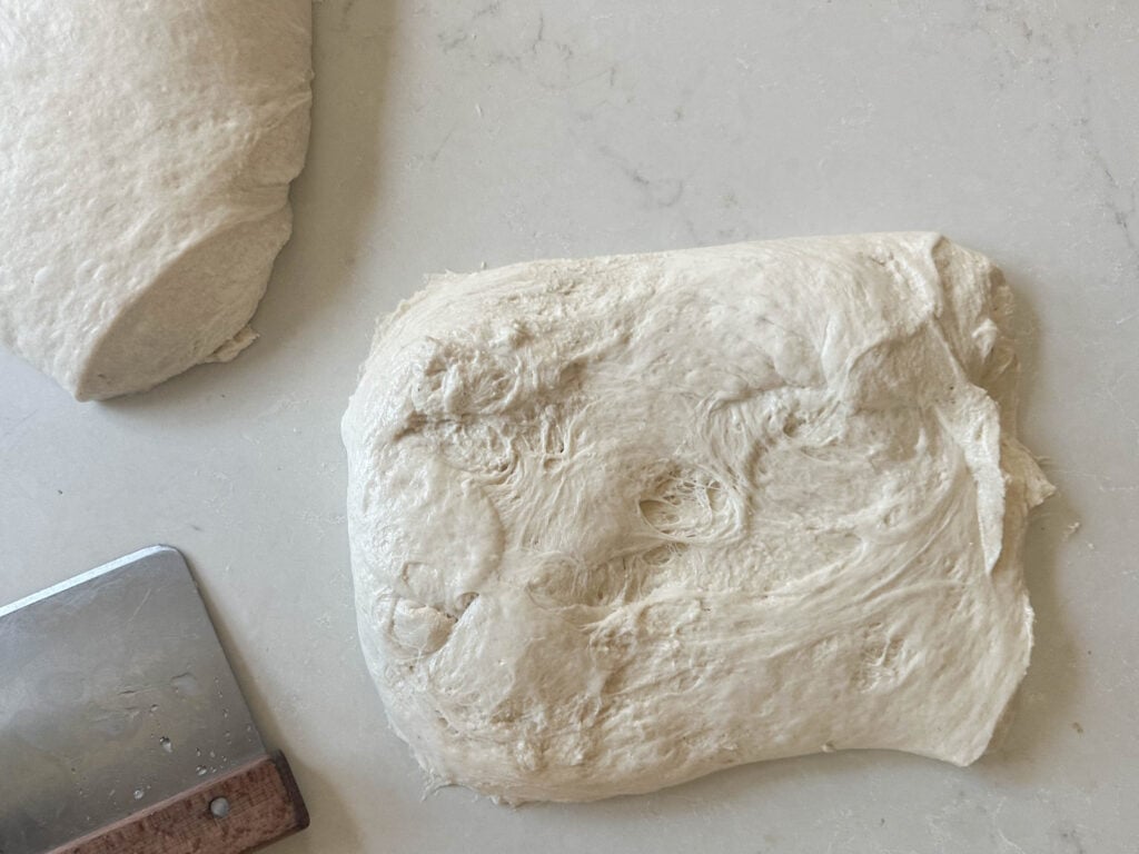 bread dough in a rectangle on a white countertop with a bench scraper to the left