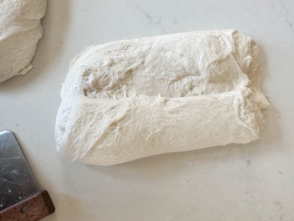 rolling up bread dough on a white countertop