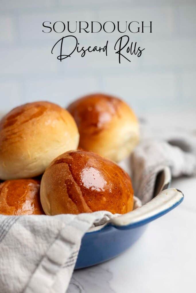 side view of soft fluffy sourdough discard rolls in a blue dish liked with a cream and blue plaid towel