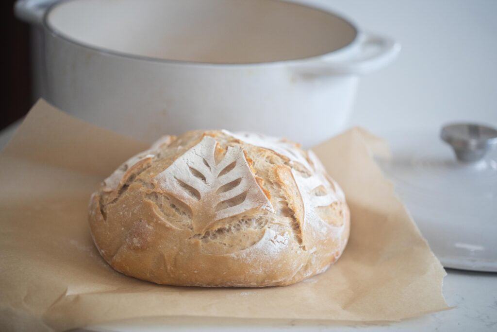 A sourdough loaf on parchment paper with a white dutch oven in the background