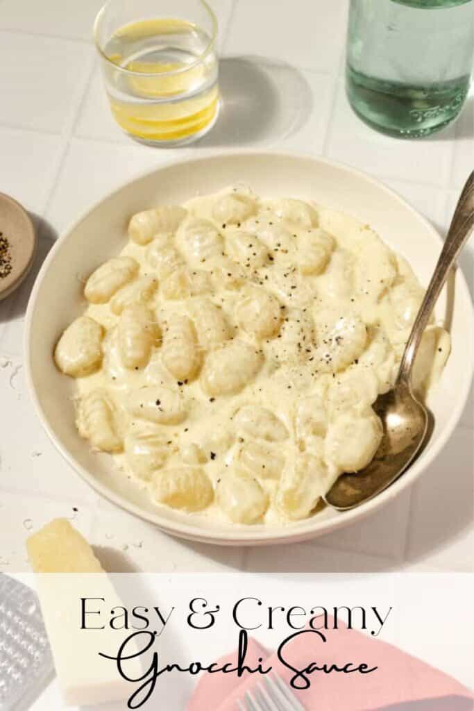 gnocchi in a creamy sauce in a bowl with a spoon. A red towel, parmesan cheese, and glasses surround the bowl