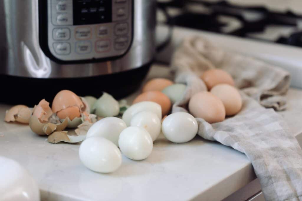 peeled and unpeeled hard boiled eggs in front of a Instant Pot on a white countertop