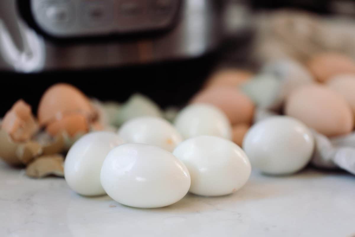 peeled hard boiled eggs on a white counter with more eggs and an Instant Pot in the background