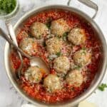 overhead photo of sausage meatballs in tomato sauce in a stainless frying pan with ingredients surrounding the pan