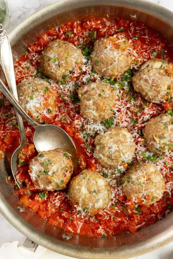 sausage meatballs in marinara sauce topped with parsley in a stainless skillet.
