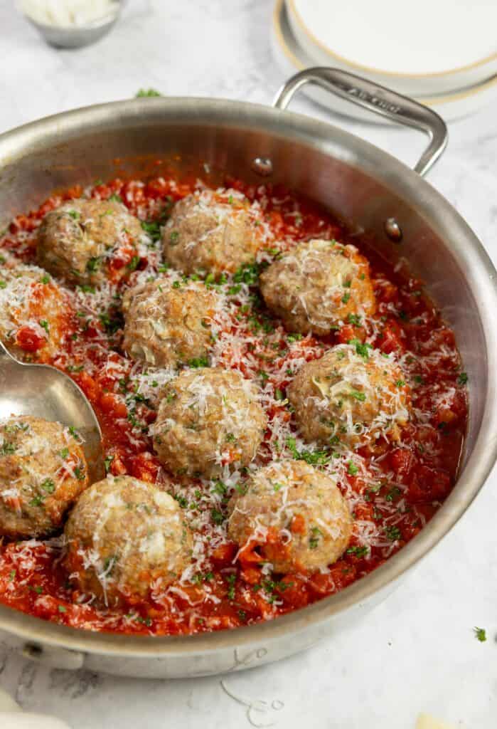10 sausage meatballs in marinara sauce topped with parsley in a stainless steel pan