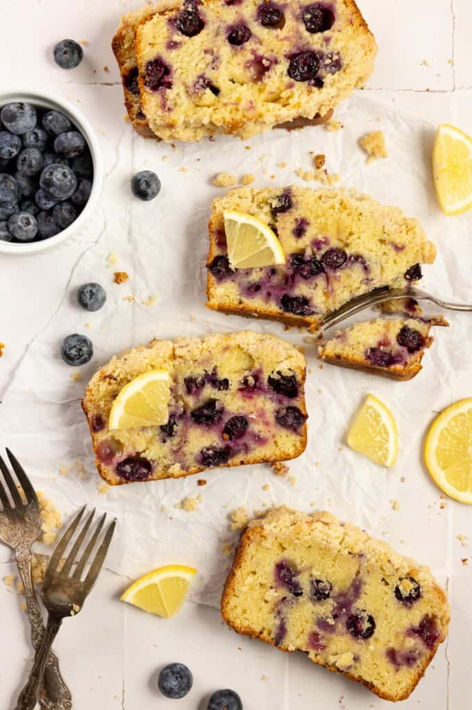 Four slices of sourdough blueberry bread with lemon slices and a bowl of blueberries on the side