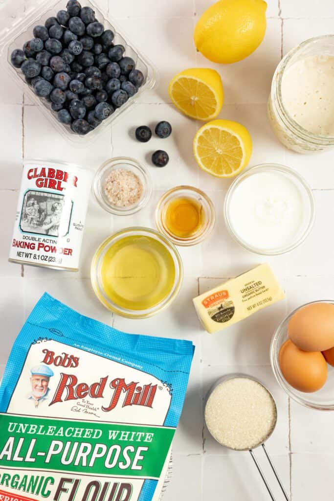 Ingredients for sourdough blueberry bread including baking powder, blueberries, lemons, salt, avocado oil, melted butter, eggs, salt, and flour