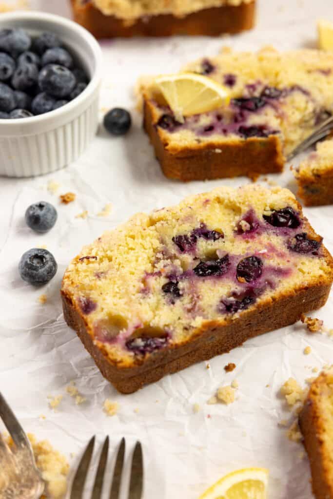 Slices of blueberry sourdough bread on a white countertop scattered with blueberries and a white dish filled with blueberries and a fork on the side