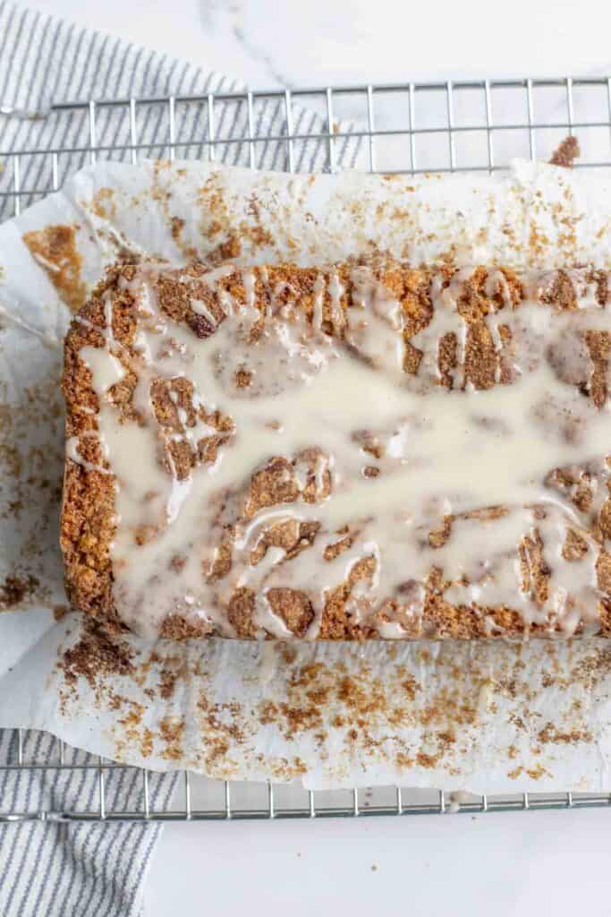 overheard photo of a loaf of sourdough cinnamon bread topped with icing on parchment paper over a cooling rack