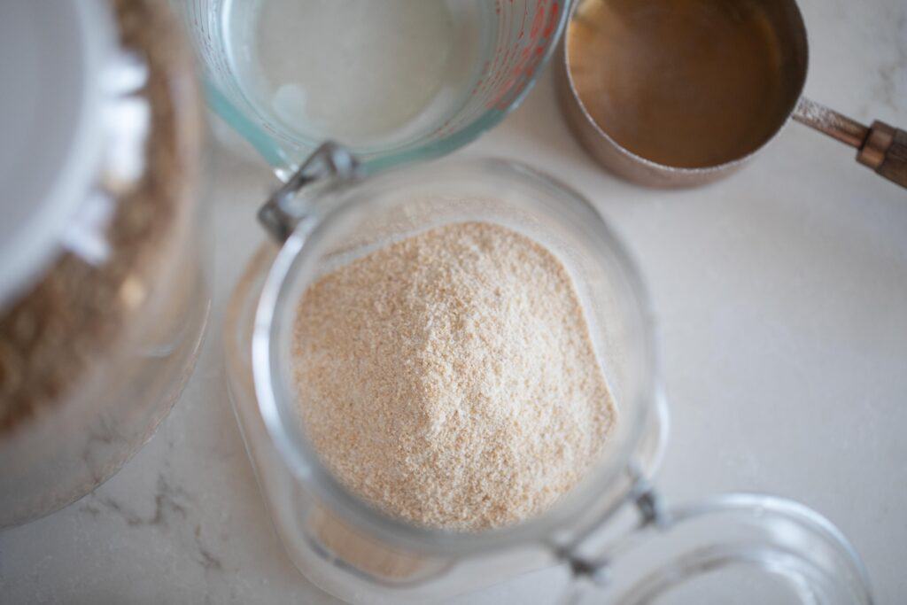 a flip top jar with flour with a measuring up and pyrex liquid measuring up of water next to the jar on a white countertop