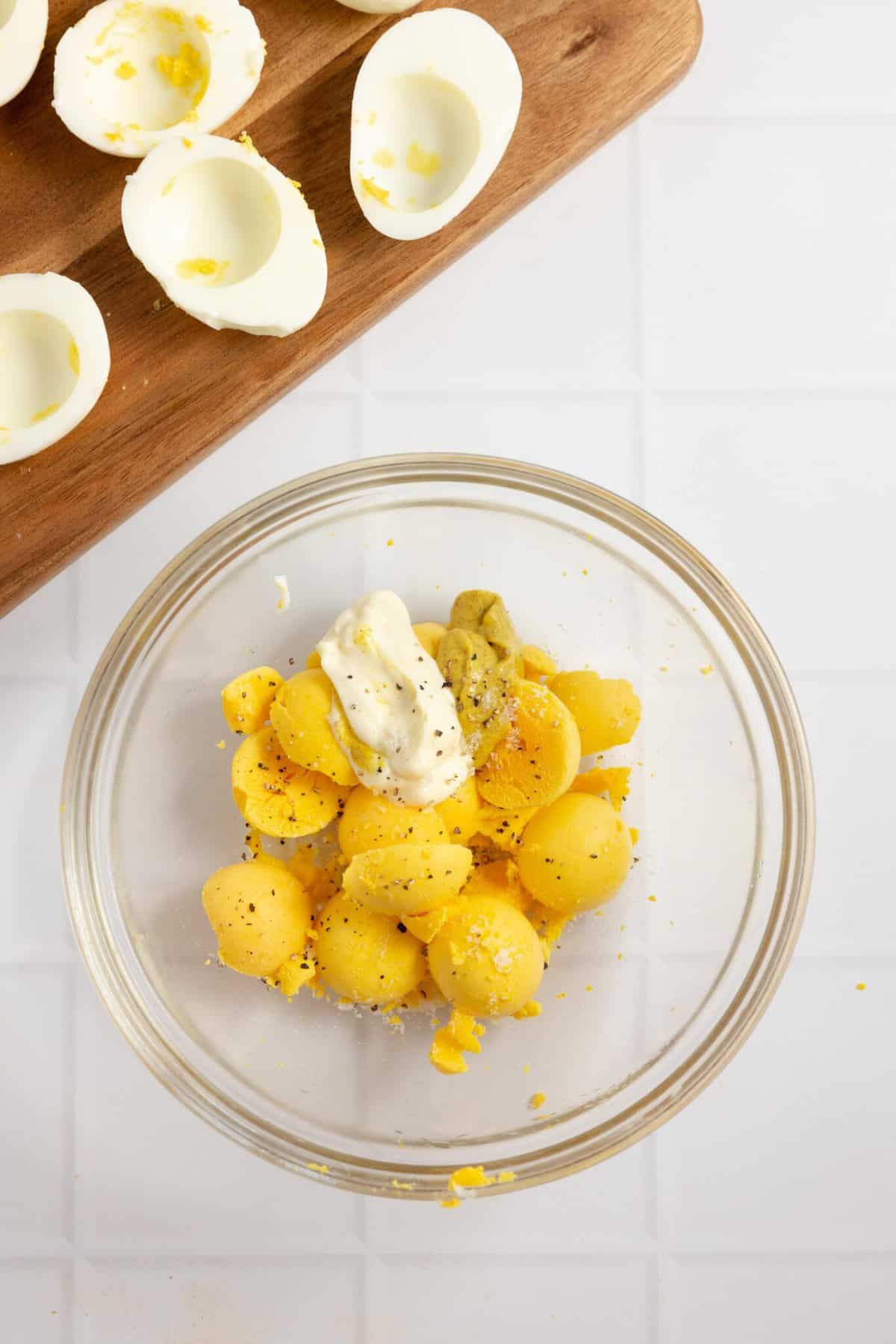 Egg yolks in a glass bowl with the remaining white on a cutting board in the background.