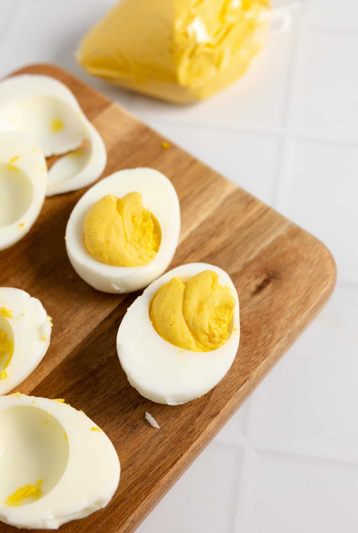 Piping egg yolk mixture into egg white on a wood cutting board.