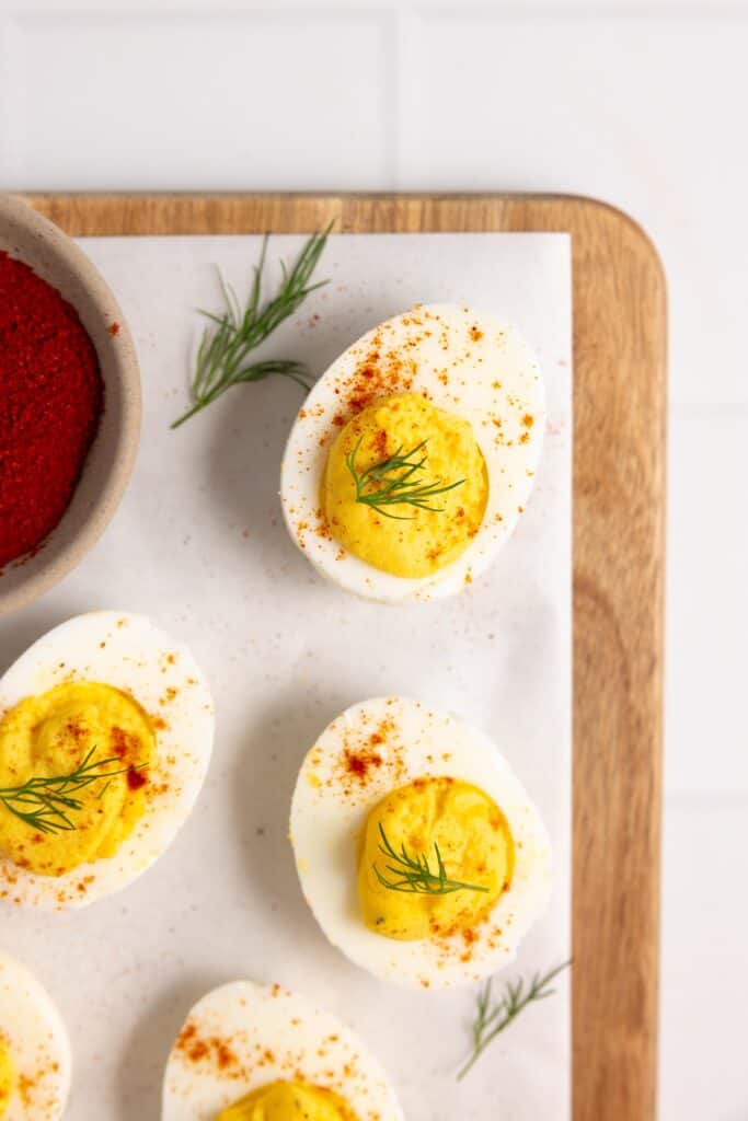 overhead photo of deviled eggs on white parchment paper on a wood cutting board