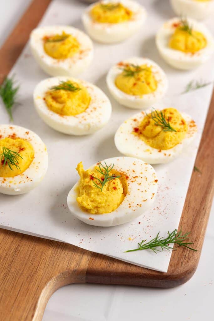 a wooden cutting board topped with parchment paper and covered in deviled eggs.