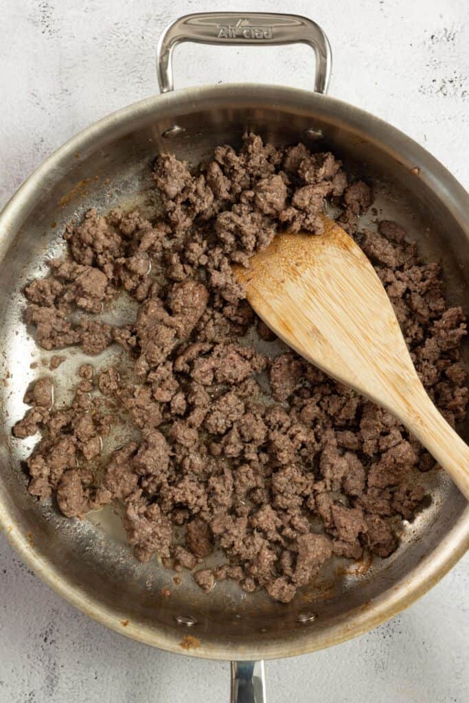 ground beef cooking in a stainless skillet with a wooden spoon