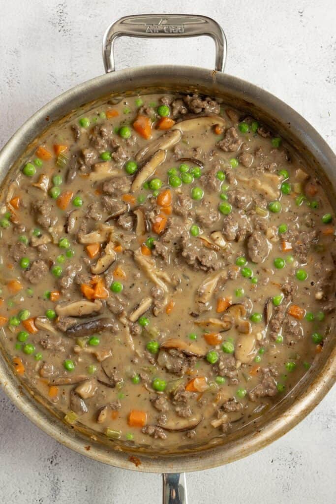 ground beef and vegetables simmering in a creamy sauce in a stainless skillet.