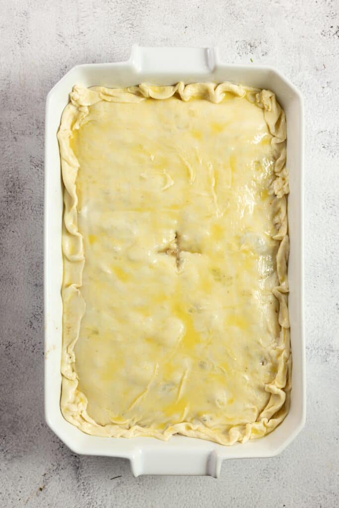 unbaked ground beef pot pie with a unbaked pie crust brushed with an egg wash in a white baking dish