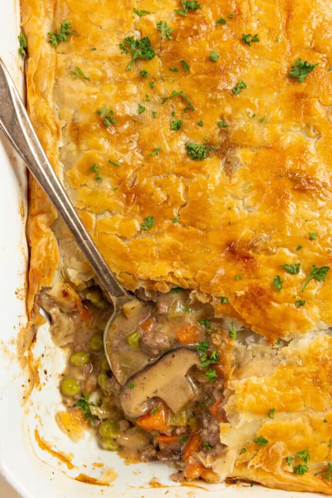 close up picture of a large serving spoon it a ground beef pot pie topped with parsley