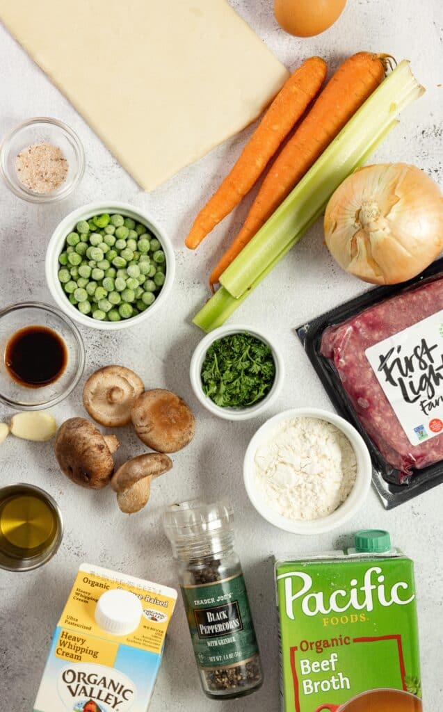 carrots, pees, onion, ground beef. mushroom, flour, cream, beef broth and herbs spread out on a countertop