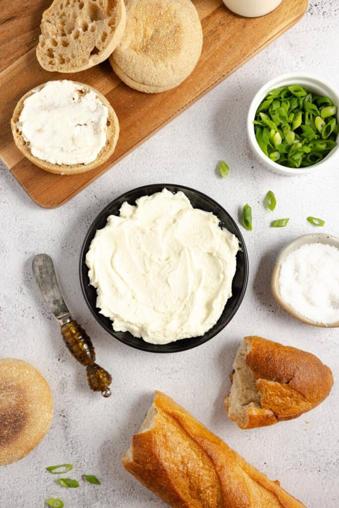 homemade cream cheese in a black bowl surrounded by bread, scallions, and a spreading knife