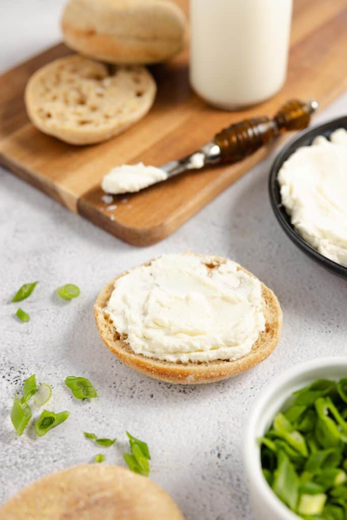homemade cream cheese on an english muffin half with a wooden cutting board and spreading knife in the background