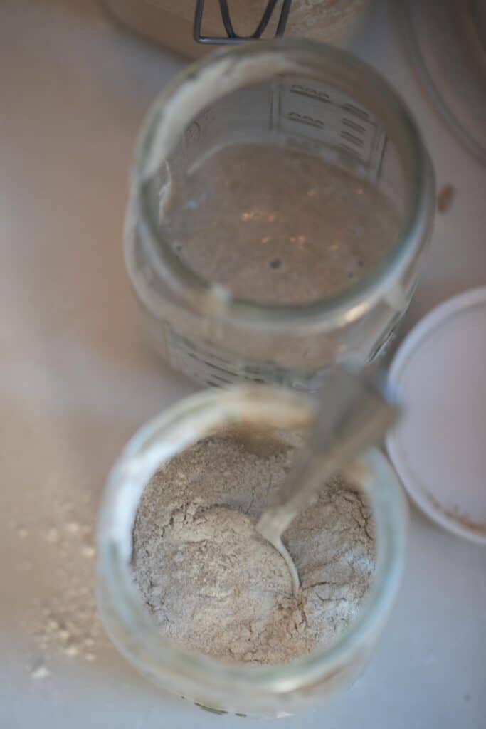 a jar of flour with a spoon with another jar of water and flour in the background